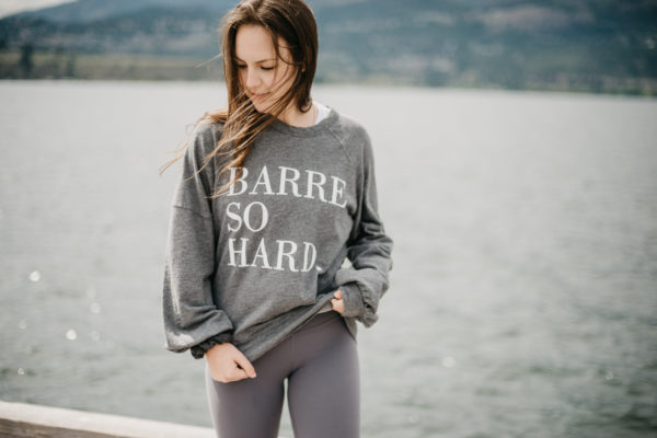 Woman in athletic wear by a lake wearing a sweatshirt representing barre workouts.